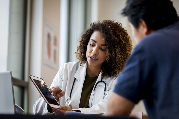 Eine Ärztin und ein Arzt besprechen sich anhand der Patientendaten auf einem Tablet.