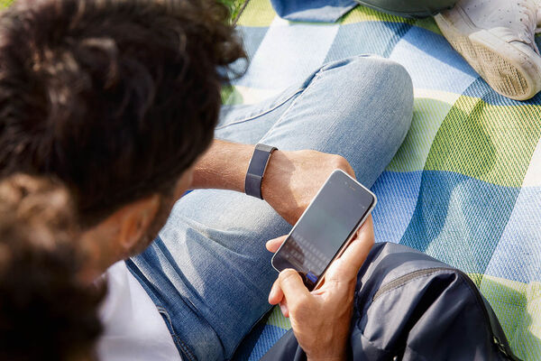 Ein Mann sitzt mit Freunden auf einer Decke im Park und tippt eine Nachricht auf seinem Handy.