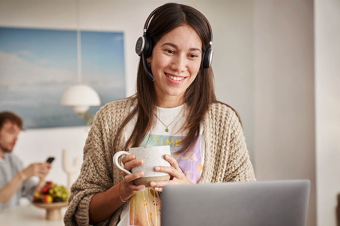 Eine Frau arbeitet im Homeoffice und nimmt gerade mit einem Headset an einer Videokonferenz teil.