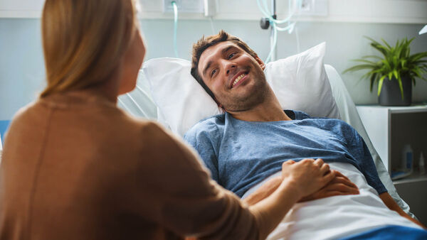 Ein junger Mann liegt im Bett im Krankenhaus und hat Besuch von seiner Freundin.