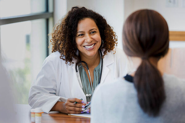 Eine Ärztin sitzt mit einer Patientin am Tisch und freut sich für sie. 