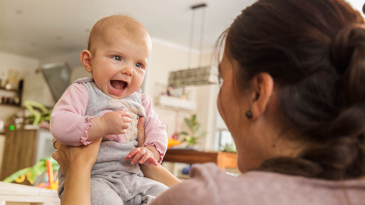 Eine Mama hält ihr Neugeborenes vor sich und sie lachen sich an.