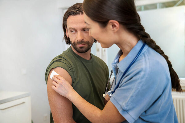 Eine Ärztin hält nach einer Impfung einen Tupfer auf die Einstichstelle am Oberarm eines Mannes.