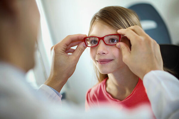 Ein Arzt kontrolliert die Brille eines Mädchens.