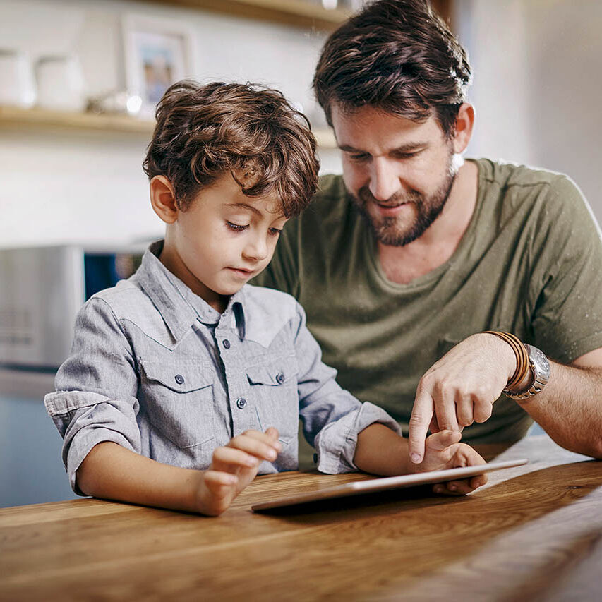 Ein Vater übt mit seinem Sohn die Benutzung des Tablets.