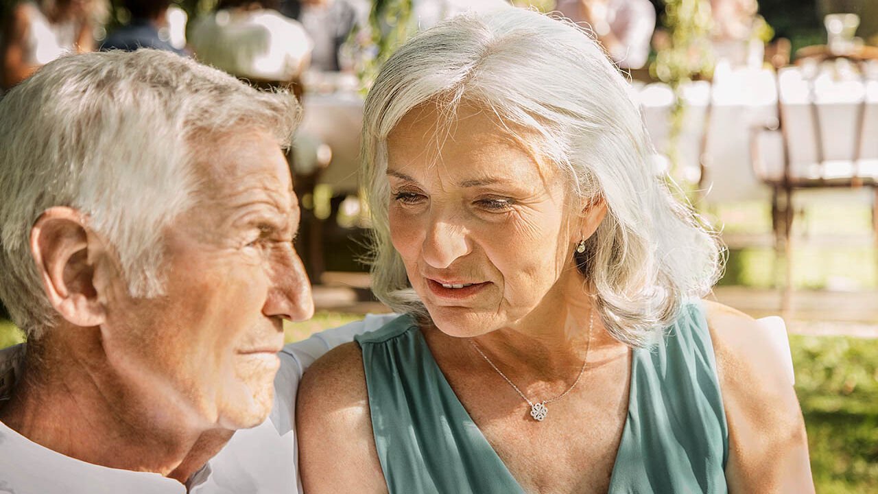 Ein älteres Paar sitzt zusammen auf einer Familienfeier und unterhält sich.