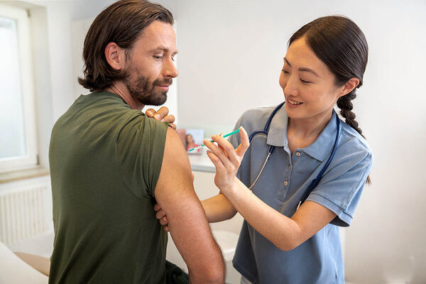 Eine Ärztin impft impft einem Mann in seinen Oberarm.