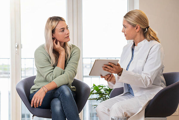 Eine Frau sitzt in einer Beratungszone der Arztpraxis und wird von ihrer Ärztin zu Vorsorgeuntersuchungen beraten.