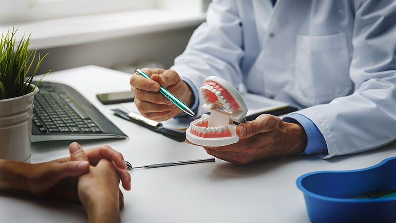 Ein Zahnarzt klärt seinen Patienten anhand eines Gebiss-Modells auf.