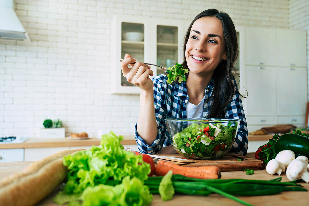 Eine Frau isst einen frischen grünen Salat in ihrer Küche. 