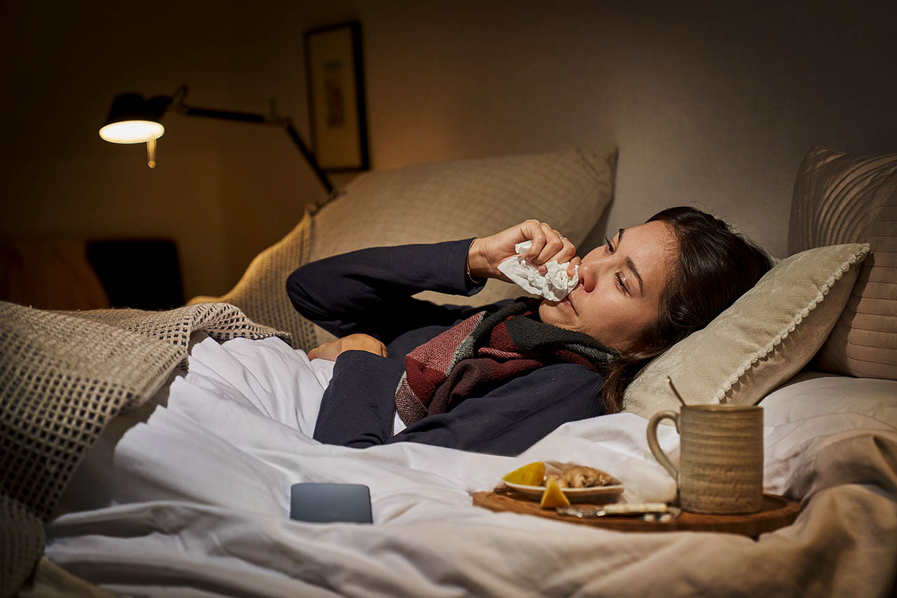 Eine Frau liegt mit einer Erkältung krank im Bett.