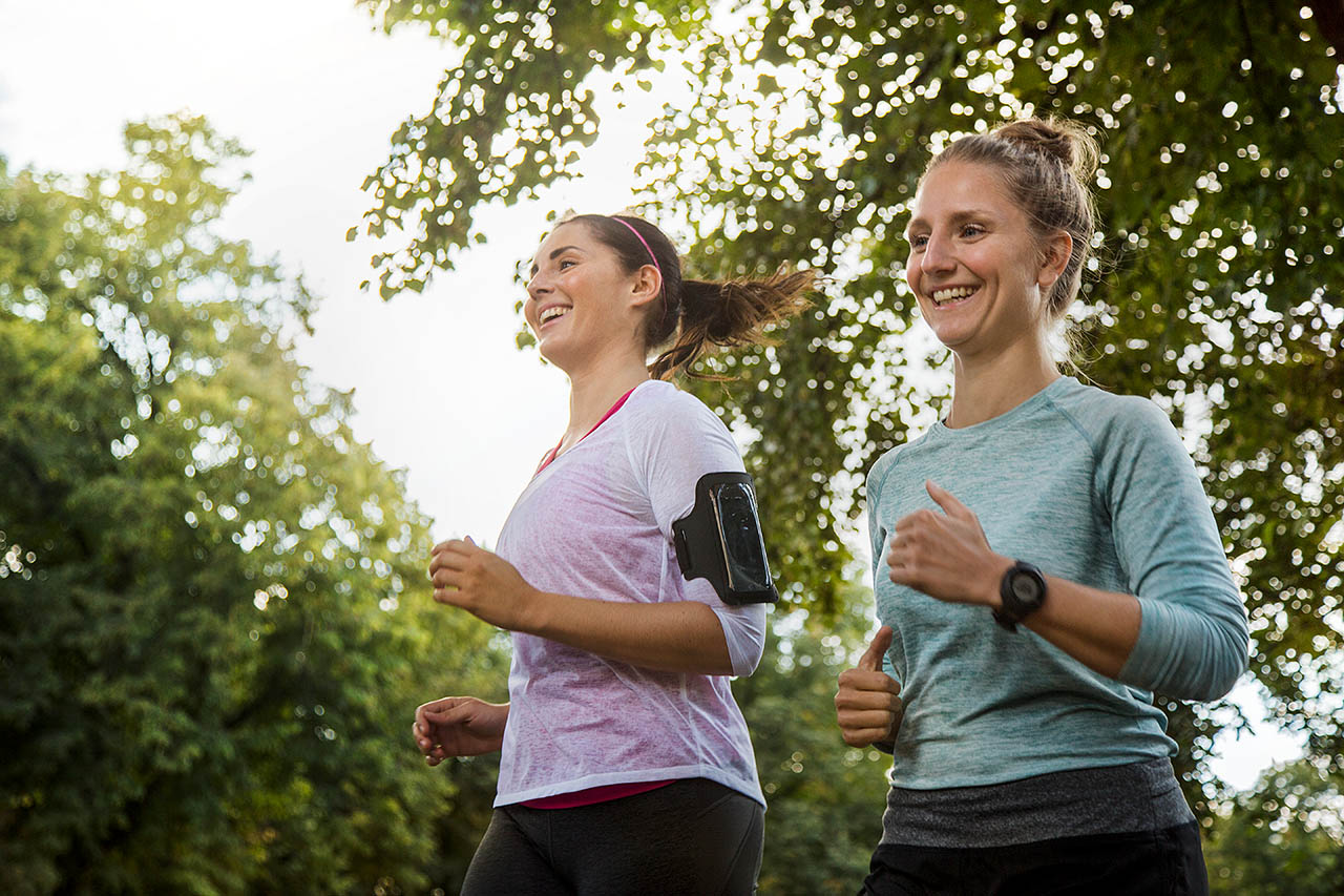 Zwei Frauen joggen gemeinsam und lachen dabei glücklich.