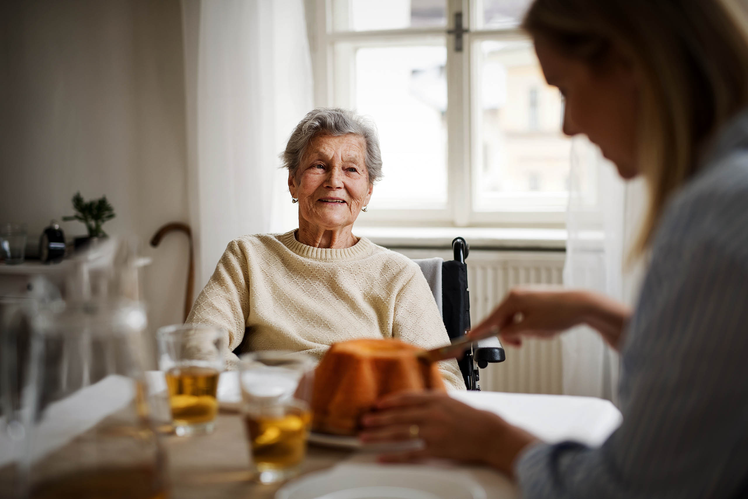 Eine ältere Dame hat Besuch von ihrer Enkelin und sie essen gemeinsam Kuchen.