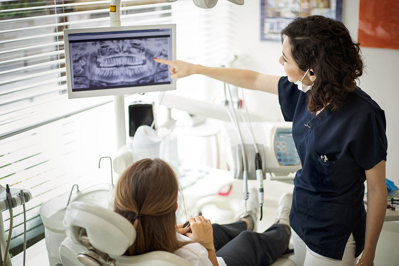 Eine Zahnärztin erklärt den Befund anhand eines Röntgenbildes einer Patientin.