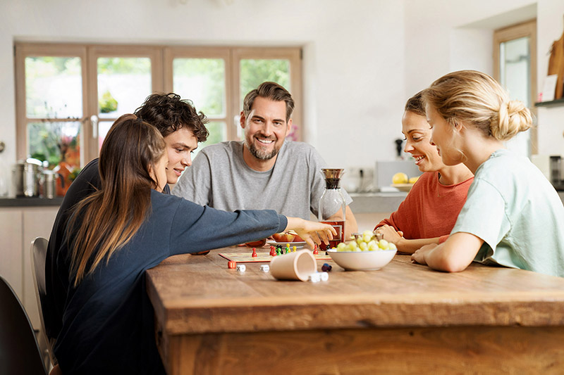 Eine Familie sitzt gemeinsam am Esstisch und spielt gemeinsam ein Spiel.