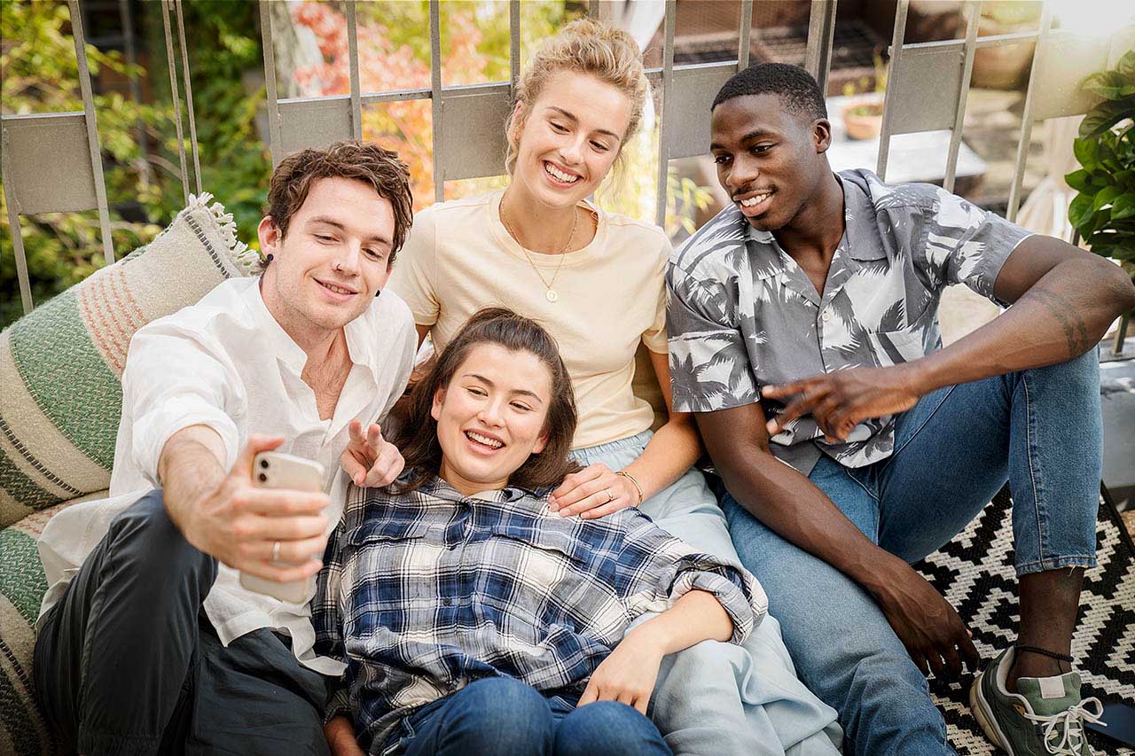 Eine Gruppe junger Erwachsener sitzt zusammen auf einem Balkon und macht ein Selfie zusammen.