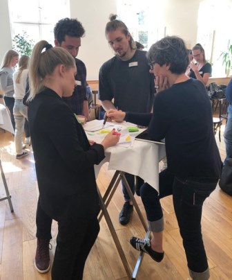 Personen stehen am Stehtisch und unterhalten sich